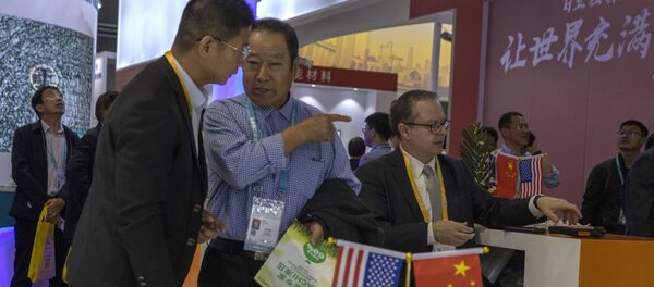 visitors chat near American and Chinese flags displayed at a booth of an American company promoting environmental sensors during the China International Import Expo in Shanghai. - 俄羅斯衛星通訊社