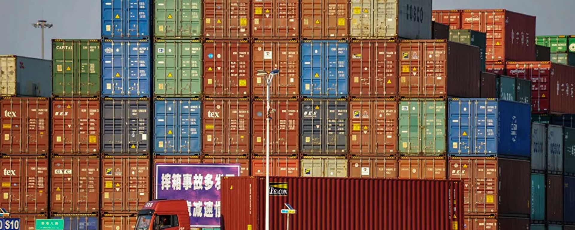 A truck transports a container next to stacked containers at a port in Qingdao in China's eastern Shandong province on October 12, 2018 - 俄羅斯衛星通訊社, 1920, 30.03.2021