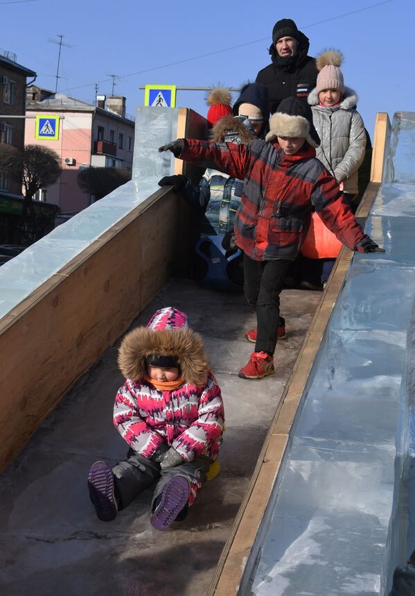 烏蘇里斯克中央廣場，市民帶著孩子們在冰雪小鎮裡玩冰滑梯 - 俄羅斯衛星通訊社