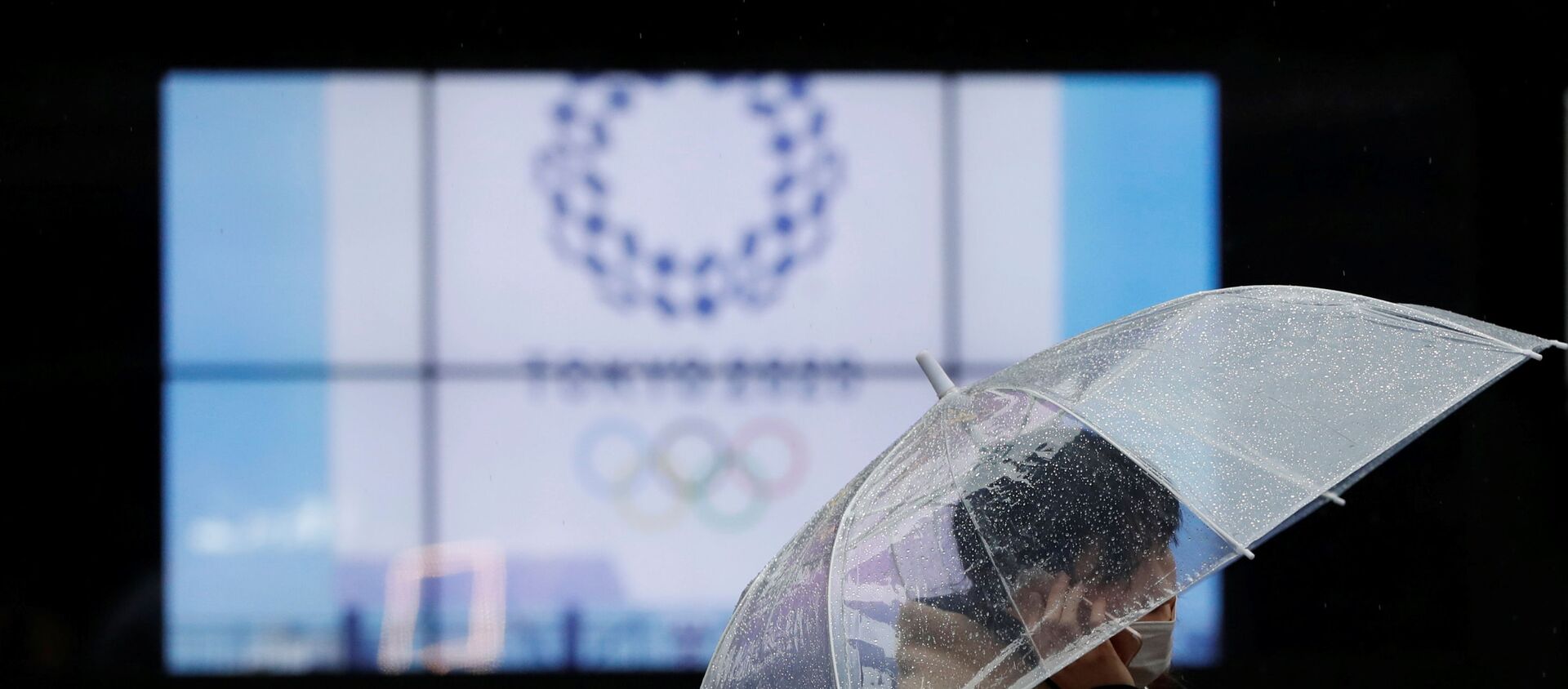 A passerby wearing a protective face mask walks past a display showing the logo of Tokyo 2020 Olympic Games that have been postponed to 2021 due to the coronavirus disease (COVID-19) outbreak, in Tokyo, Japan January 23, 2021. - 俄罗斯卫星通讯社, 1920, 08.02.2021