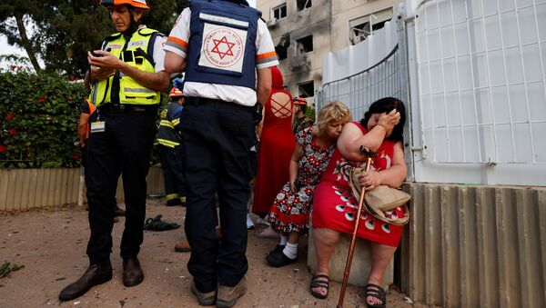 Израильские медики стоят рядом с женщинами возле дома, поврежденного ракетой, запущенной из сектора Газа в Ашкелоне - 俄羅斯衛星通訊社