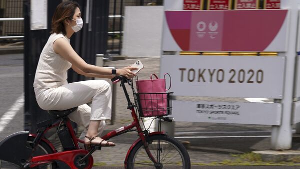 Женщина в защитной маске проезжает на велосипеде мимо баннера Олимпийских и Паралимпийских игр в Токио  - 俄罗斯卫星通讯社