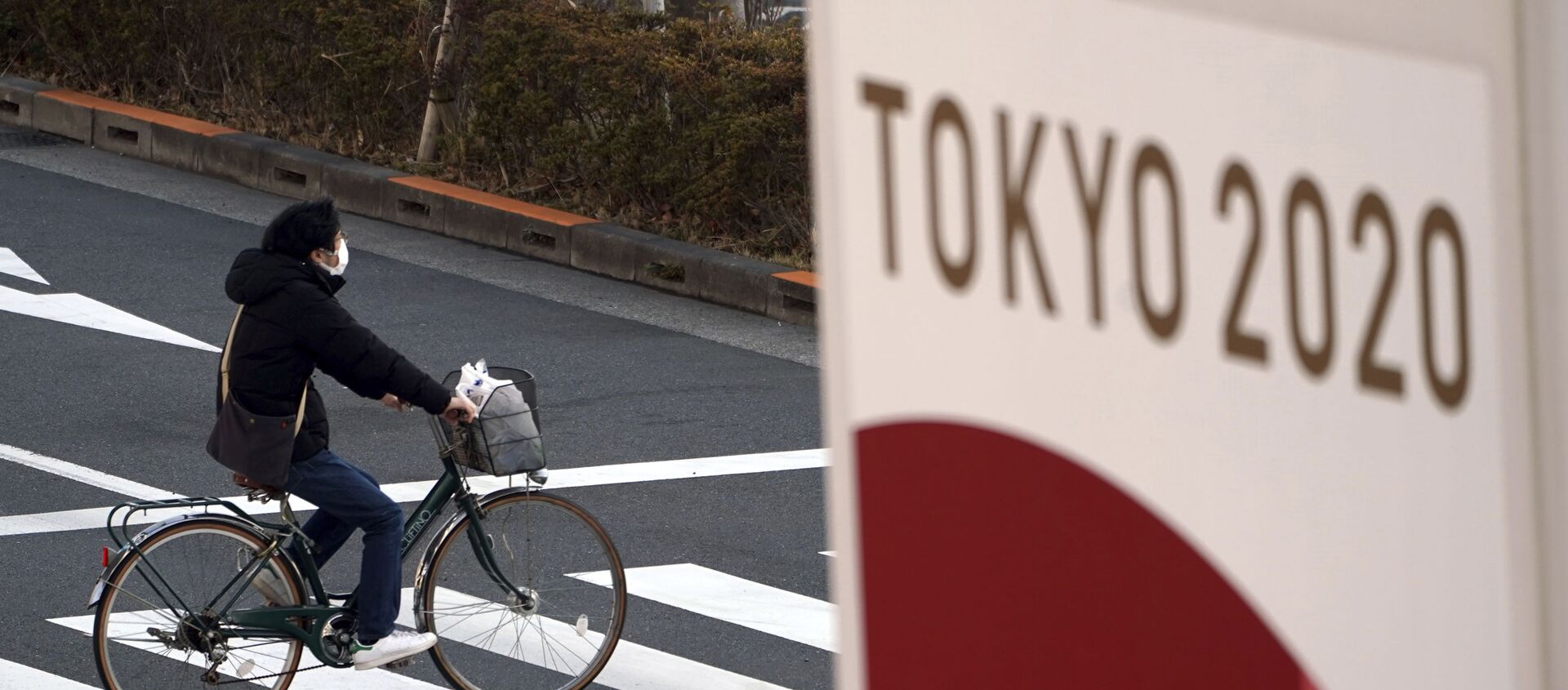 Велосипедист в защитной маске на фоне баннера Олимпиады 2020 в Токио - 俄羅斯衛星通訊社, 1920, 17.06.2021