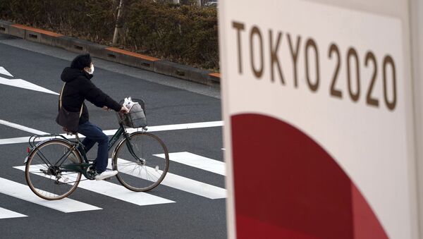 Велосипедист в защитной маске на фоне баннера Олимпиады 2020 в Токио - 俄羅斯衛星通訊社