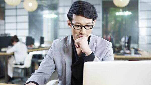 Азиатский мужчина за ноутбуком в офисе  - 俄罗斯卫星通讯社