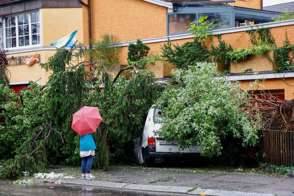 Женщина стоит перед фургоном, поврежденным упавшим деревом во время грозы и проливного дождя в Цюрихе, Швейцария - 俄羅斯衛星通訊社