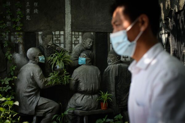 一位佩戴口罩的北京市民路过一处雕塑。 - 俄罗斯卫星通讯社
