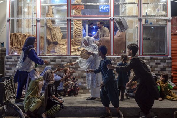 一名婦女在喀布爾一家麵包店門口向貧困兒童分發麵包。 - 俄羅斯衛星通訊社