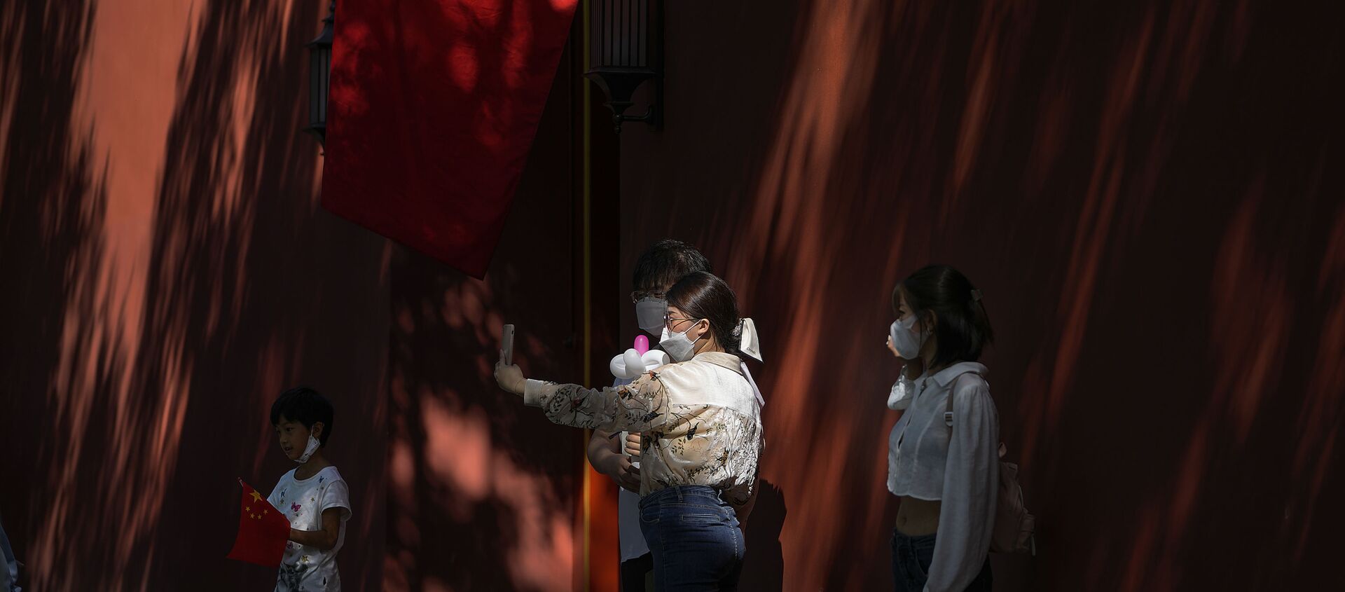 A couple wearing face masks to help protect from the coronavirus pose for a selfie near a national flag on a wall cast with shadows from trees on National Day in Beijing, Friday, Oct. 1, 2021. Hundreds of thousands domestic tourists flock to the square to celebrate the 72nd National Day of the People's Republic of China over a week-long holiday. (AP Photo/Andy Wong) - 俄羅斯衛星通訊社, 1920, 02.10.2021