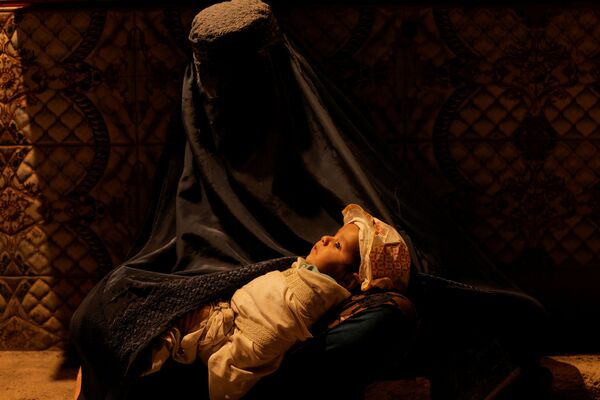 喀布爾，一名身著布爾卡長袍的女子懷抱嬰兒坐在麵包房附近。 - 俄羅斯衛星通訊社