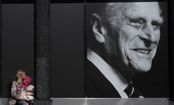 英國菲利普親王病逝。圖為伊莎貝拉與小狗可可在溫莎百貨商場櫥窗外觀看巨幅宣傳畫。 - 俄羅斯衛星通訊社