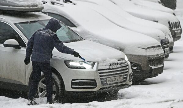 下雪时，一名男子在清扫私家车上的积雪。 - 俄罗斯卫星通讯社