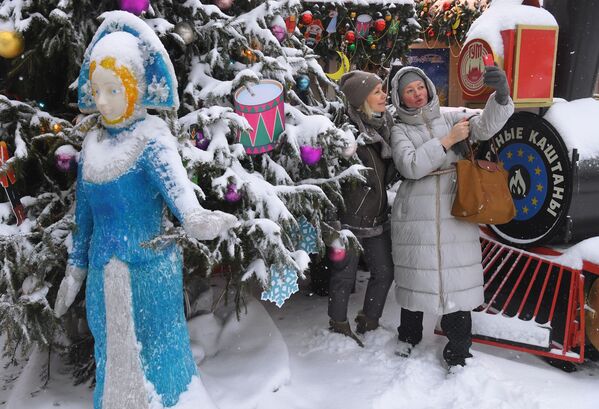 下雪時，姑娘們在古姆百貨商場附近的新年樅樹前拍照。 - 俄羅斯衛星通訊社