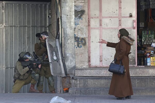 約旦河西岸城市希伯倫，一名婦女向正在驅散投擲石塊的巴勒斯坦人的以色列安全部隊做手勢，2022年2月9日。 - 俄羅斯衛星通訊社