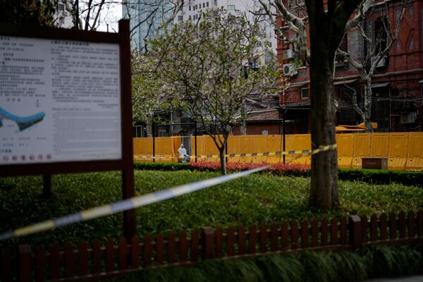 上海新冠疫情期间，一名身穿防护服的工作人员坐在黄色围挡的一个社区入口处，2022年3月26日。 - 俄罗斯卫星通讯社