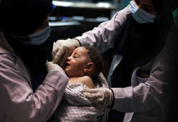 一名护士抱着奥马尔·哈迪迪，他被从瓦砾中救出，而她的其他七名家庭成员，在2021年5月15日以色列在没有事先警告的情况下对在加沙的沙地难民营进行了夜间空袭后，在什法医院去世。5月14日，以色列面临着不断扩大的冲突。在加沙地带遭遇大规模空袭的同时，约旦河西岸爆发了致命的暴力事件，该国境内的阿拉伯人和犹太人出现了前所未有的动荡。约旦河西岸的冲突被认为是自2000年开始的第二次起义以来最激烈的冲突之一。巴勒斯坦卫生部表示，以色列的炮火导致11人死亡，加沙地带空袭造成的总死亡人数上升到126人。 - 俄罗斯卫星通讯社