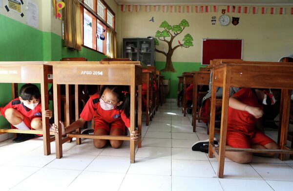 2022年5月24日，在印度尼西亚巴厘岛举行的地震海啸应急演习中，小学生们在课桌下躲避。 - 俄罗斯卫星通讯社