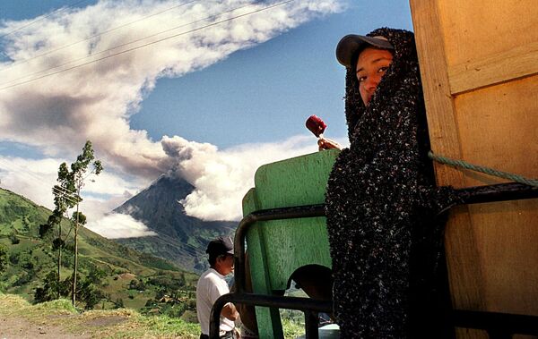 1999年11月11日，在南美洲厄瓜多爾，一名婦女吃著冰淇淋，旁邊的通古拉瓦火山正在噴吐著火山灰和煙霧。 - 俄羅斯衛星通訊社