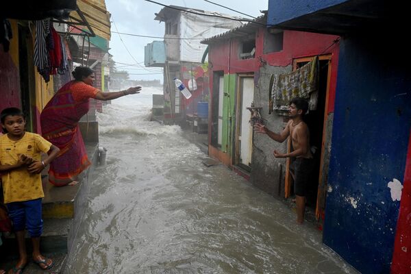 2022年6月15日，孟买涨潮时，海水涌入海滨附近的住宅区，一位居民（左）将一瓶饮用水扔给她的邻居。 - 俄罗斯卫星通讯社