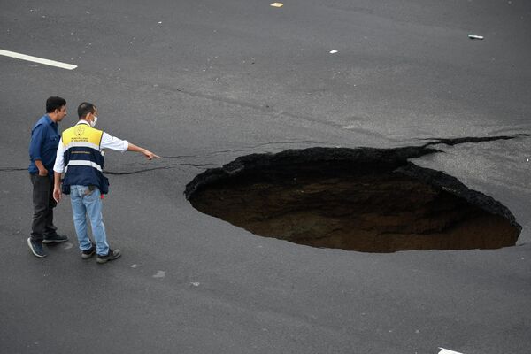 2022年6月14日，在危地馬拉城南部15公里處的Villa Nueva，兩名市政人員盯著道路上一個巨大的洞，這個洞是由於全國大雨導致的排水系統崩潰造成的。 - 俄羅斯衛星通訊社