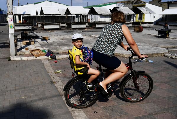 沃尔诺瓦哈市场边，一名妇女带着孩子骑着自行车。 - 俄罗斯卫星通讯社