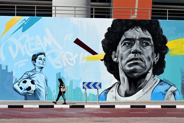 11月18日，2022年卡塔爾世界杯開幕前夕，一名女子在多哈哈利發國際體育場附近路過一幅描繪阿根廷傳奇球星馬拉多納的壁畫。 - 俄羅斯衛星通訊社