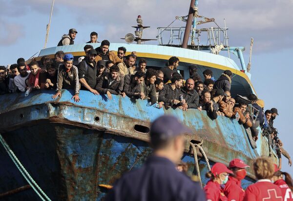 2022年11月22日，移民從一艘停靠在希臘克里特島東南部港口的漁船上向外看。希臘當局表示，一艘擠滿了數百名移民的漁船失去了方向，一直在希臘克里特島南部的地中海漂流，現已被成功拖到港口。目前沒有任何關於人員受傷或失蹤的報告。 - 俄羅斯衛星通訊社