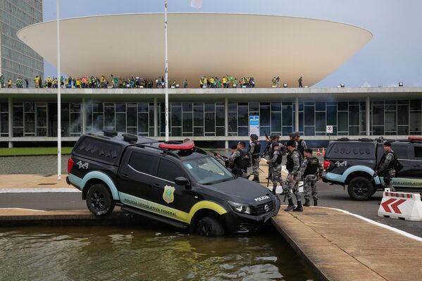 1月8日，巴西前总统博索纳罗的支持者在闯入位于巴西利亚的国民议会时，联邦议会警察站在一辆撞上喷泉的车辆旁边。 - 俄罗斯卫星通讯社