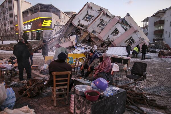 受灾民众站在土耳其南部阿德亚曼省戈尔巴西区倒塌的建筑物旁。 - 俄罗斯卫星通讯社