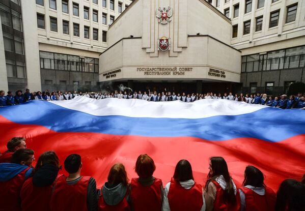 參加克里米亞入俄週年紀念日活動的人們，在克里米亞共和國國務委員會前的廣場上展示巨大的俄羅斯國旗 - 俄羅斯衛星通訊社