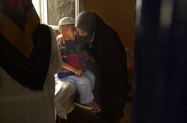 2001年1月15日，8 岁的艾哈迈德·拉迪在伊拉克的加兹万儿童医院等待接受每周一次的化疗，母亲正在安慰他。 拉迪先天失明，七岁时患上脑瘤。伊拉克政府称，海湾战争期间，该地被美国投放大量贫铀弹。 - 俄罗斯卫星通讯社