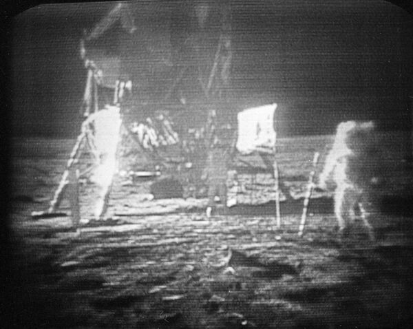 1969年7月20日，阿波罗11号宇航员尼尔·阿姆斯特朗（右）艰难地走过月球表面，身后是他留下的脚印。 宇航员在阿姆斯特朗和登月舱之间的月球表面插上美国国旗。 宇航员埃德温·E·奥尔德林离飞船更近。 - 俄罗斯卫星通讯社