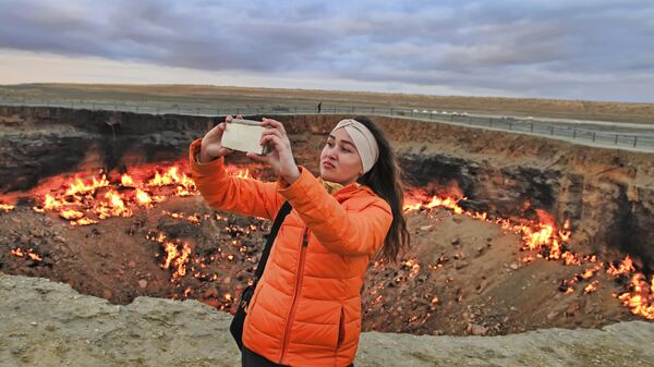 一名女孩站在土庫曼斯坦卡拉庫姆沙漠燃燒的火山口“地獄之門”前自拍。 - 俄羅斯衛星通訊社