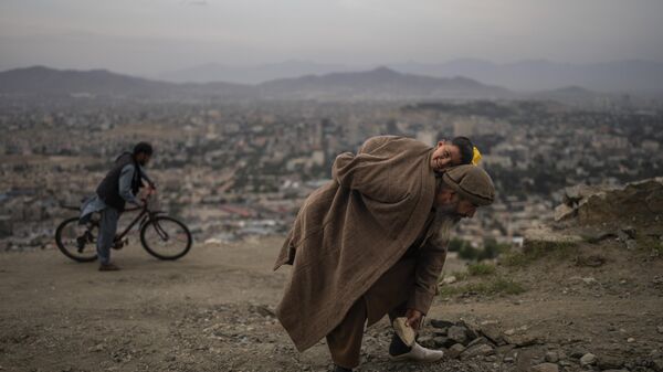 Абдул Кадер Газизада убирает камни с дороги, неся на руках своего 2-летнего сына, Афганистан - 俄羅斯衛星通訊社