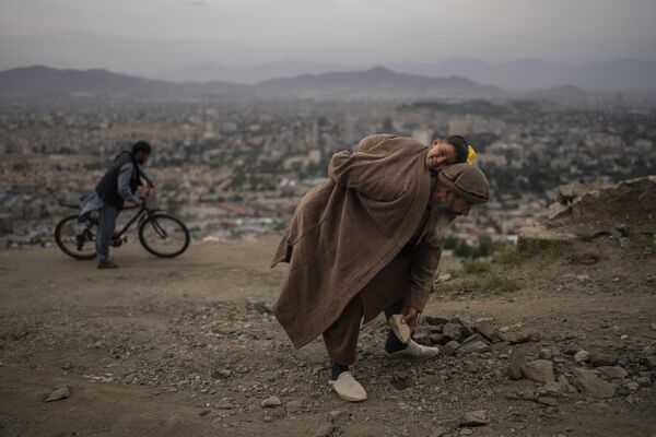 阿富汗居民阿卜杜勒·卡德爾·加濟扎達背著2歲的兒子清理路上的石頭。 - 俄羅斯衛星通訊社