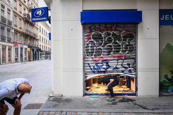 7月1日，法国里昂市，一名行人（左）看着一名员工（右）进入一家被抢劫的商店。 - 俄罗斯卫星通讯社