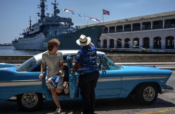 古巴游客从一辆经典的美国汽车里下车。远景为俄罗斯海军“佩雷科普”号训练舰。 - 俄罗斯卫星通讯社