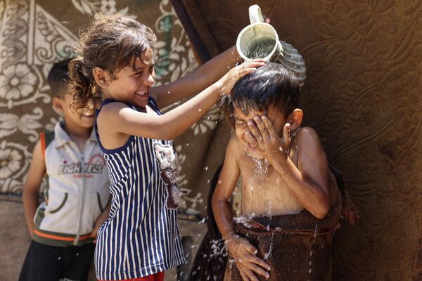 加沙市连日来气温急剧上升，市内又遇停电。图为一女孩正在给男孩泼水降温。 - 俄罗斯卫星通讯社