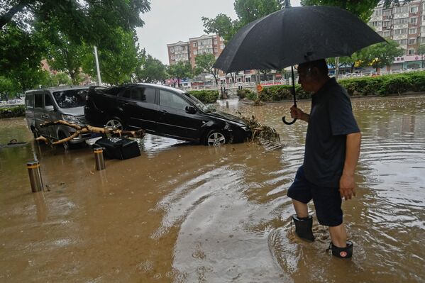 2023年7月31日，北京門頭溝區，暴雨過後，一名男子涉水經過一條被洪水淹沒的街道上一輛受損的汽車。(Pedro PARDO/法新社） - 俄羅斯衛星通訊社