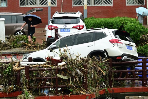 2023年7月31日，北京門頭溝區，一名男子在暴雨後從一輛受損汽車旁走過。(Pedro PARDO/法新社） - 俄羅斯衛星通訊社