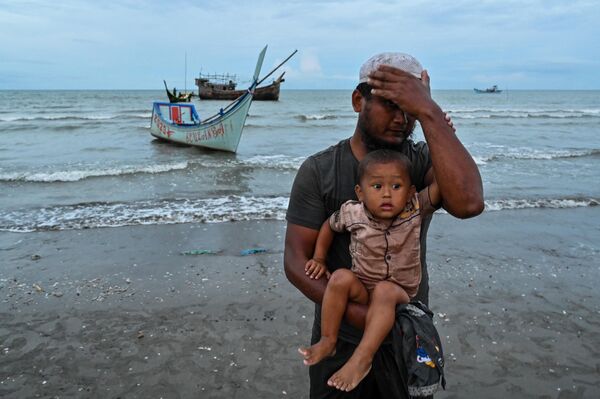 一名新到達印度尼西亞亞齊省一海灘的羅興亞難民，他在到達後抱著嬰兒捂著頭的樣子。 - 俄羅斯衛星通訊社