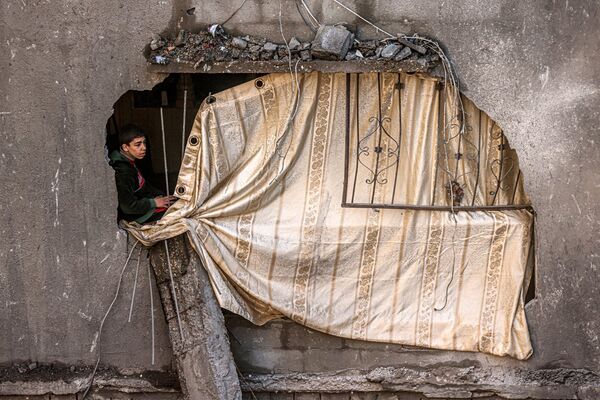 加沙地帶拉法，在一棟被以色列轟炸摧毀的建築內，一個男孩坐在用粗布蓋住的牆洞內。 - 俄羅斯衛星通訊社