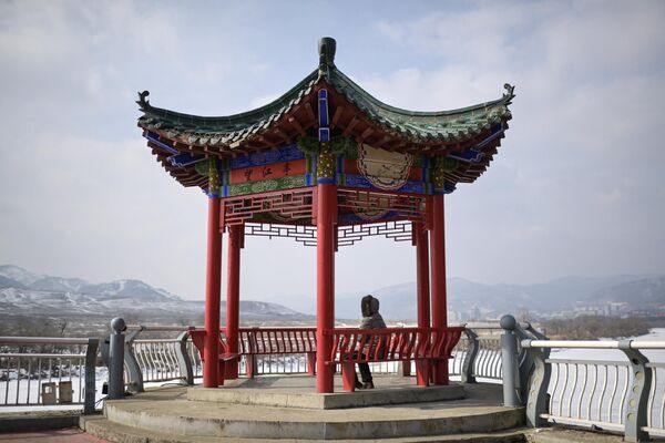 2024年2月29日，吉林省臨江市一位婦女坐在亭子長凳上看向朝鮮中江郡。 - 俄羅斯衛星通訊社