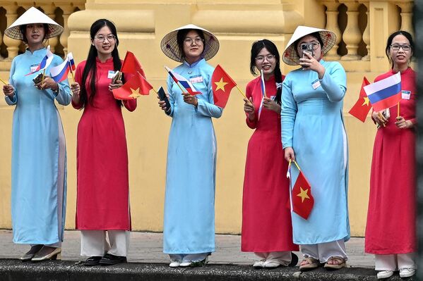 身着越南传统“奥黛”服饰的女子在河内主席府外挥舞着越南和俄罗斯国旗，等候普京到来。 - 俄罗斯卫星通讯社