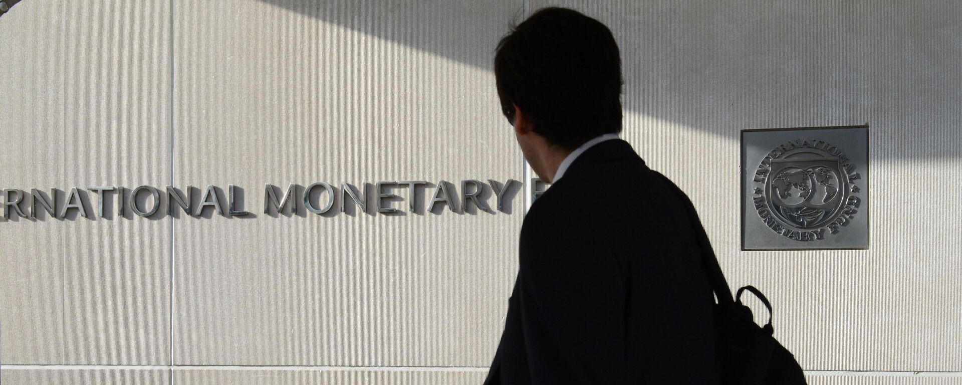 Мужчина у здания Международного валютного фонда смотрит на логотип МВФ на стене. - 俄罗斯卫星通讯社, 1920, 25.07.2025