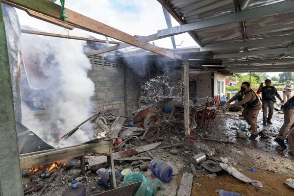 2025年12月11日，泰国素林府，一名泰国警察正在泼水扑灭房屋火灾。据泰国地方安全部队称，该房屋系被柬埔寨炮火击中受损。 - 俄罗斯卫星通讯社