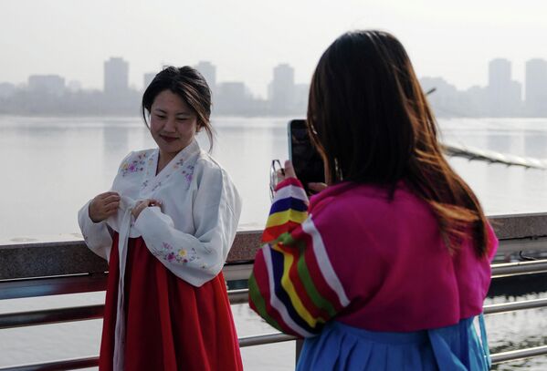 2026年1月15日，在中国辽宁省丹东市，穿着传统朝鲜服饰的游客在分隔中国和朝鲜的鸭绿江岸边拍照，背景中可见朝鲜新义州的建筑。 - 俄罗斯卫星通讯社