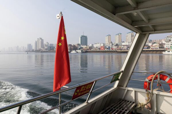 2026年1月15日，中国辽宁省丹东市，一艘中国国旗的旅游船在鸭绿江上航行，该江将中国和朝鲜分隔开，背景是丹东市的天际线。 - 俄罗斯卫星通讯社