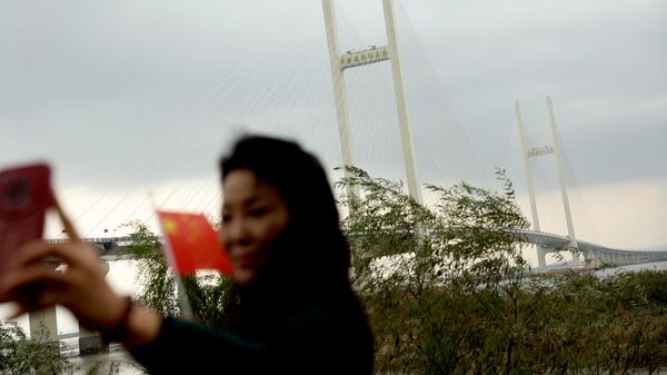 一位女士在中朝新鸭绿江大桥前与中国国旗合影  - 俄罗斯卫星通讯社