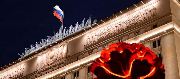 Флаг на здании министерства обороны РФ на Фрунзенской набережной в Москве с вечерней подсветкой. Справа - инсталляция к Дню Победы в виде цветка гвоздики - 俄罗斯卫星通讯社